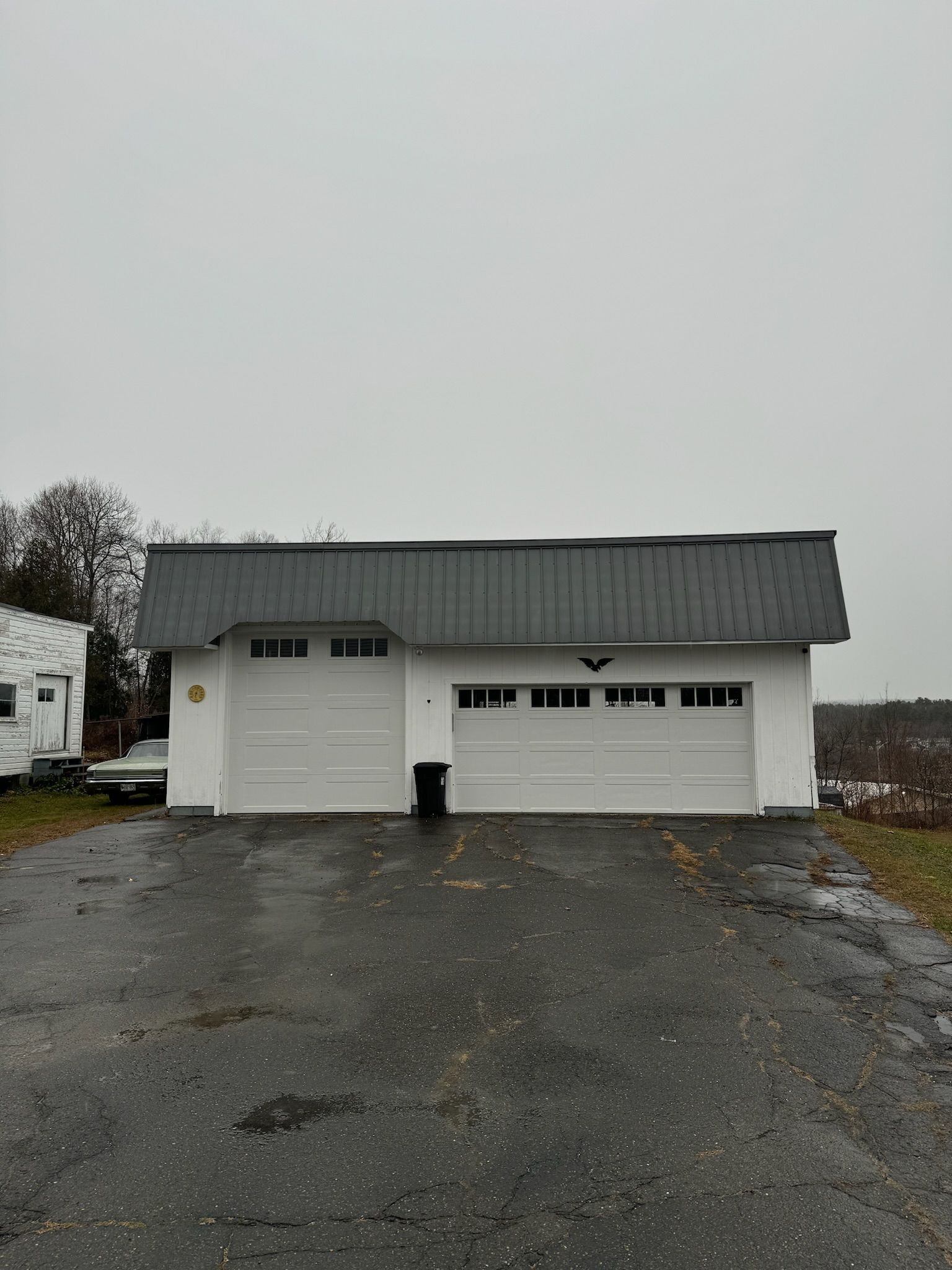 A white garage with a gray roof is sitting on the side of a road.
