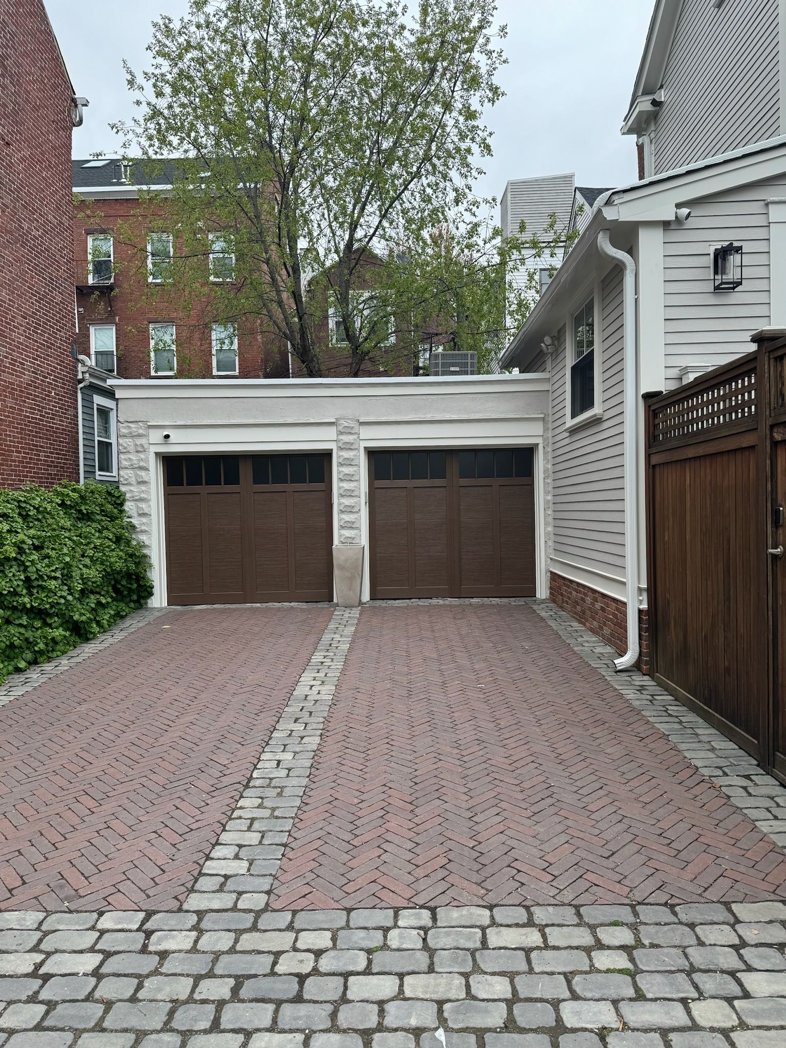 A brick driveway leading to two garage doors next to a house.