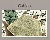A hand holding a light tan Gabian rock. Green and white rocks are in the background.