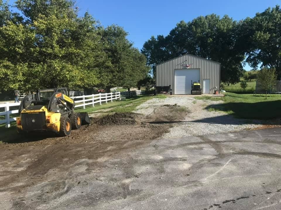 A yellow tractor is driving down a dirt road in front of a barn.