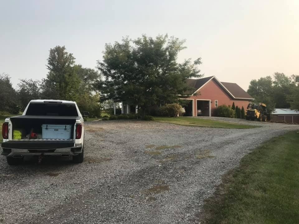 A white truck is parked in a gravel driveway in front of a house.