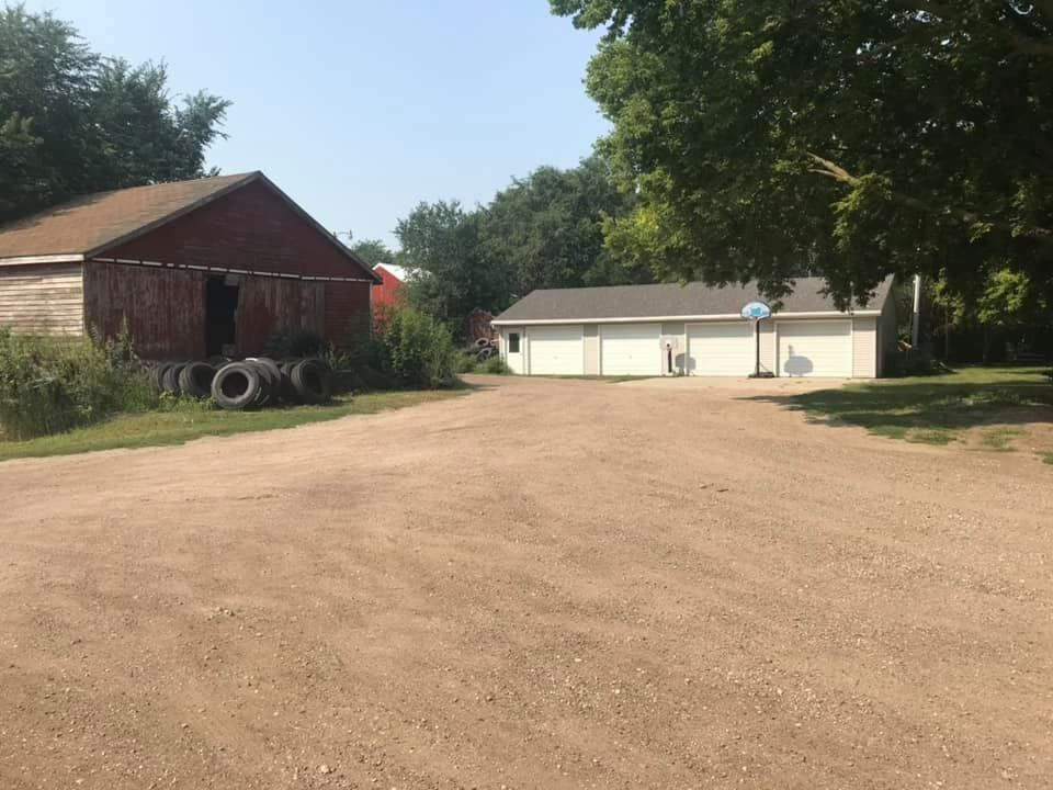 A dirt road leading to a house with a red barn in the background