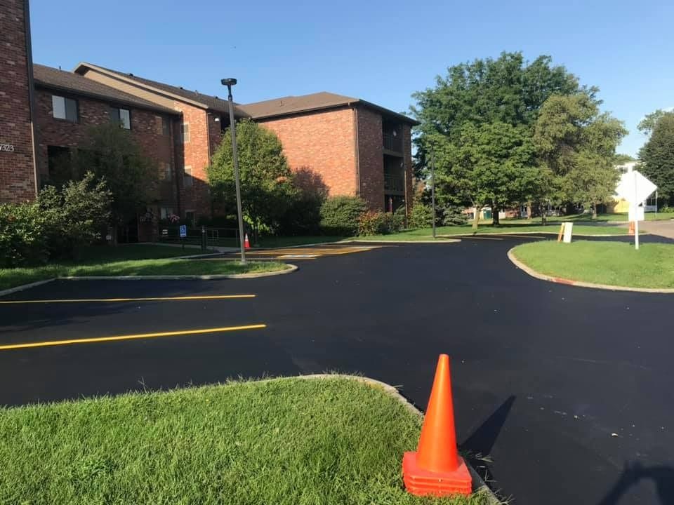 A parking lot with a brick building in the background and an orange cone in the foreground.
