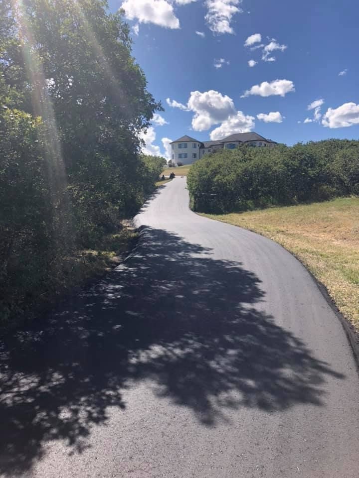 A road with trees on both sides and a house in the background.