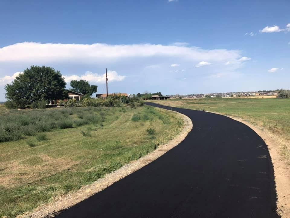 A road going through a grassy field with a house in the background