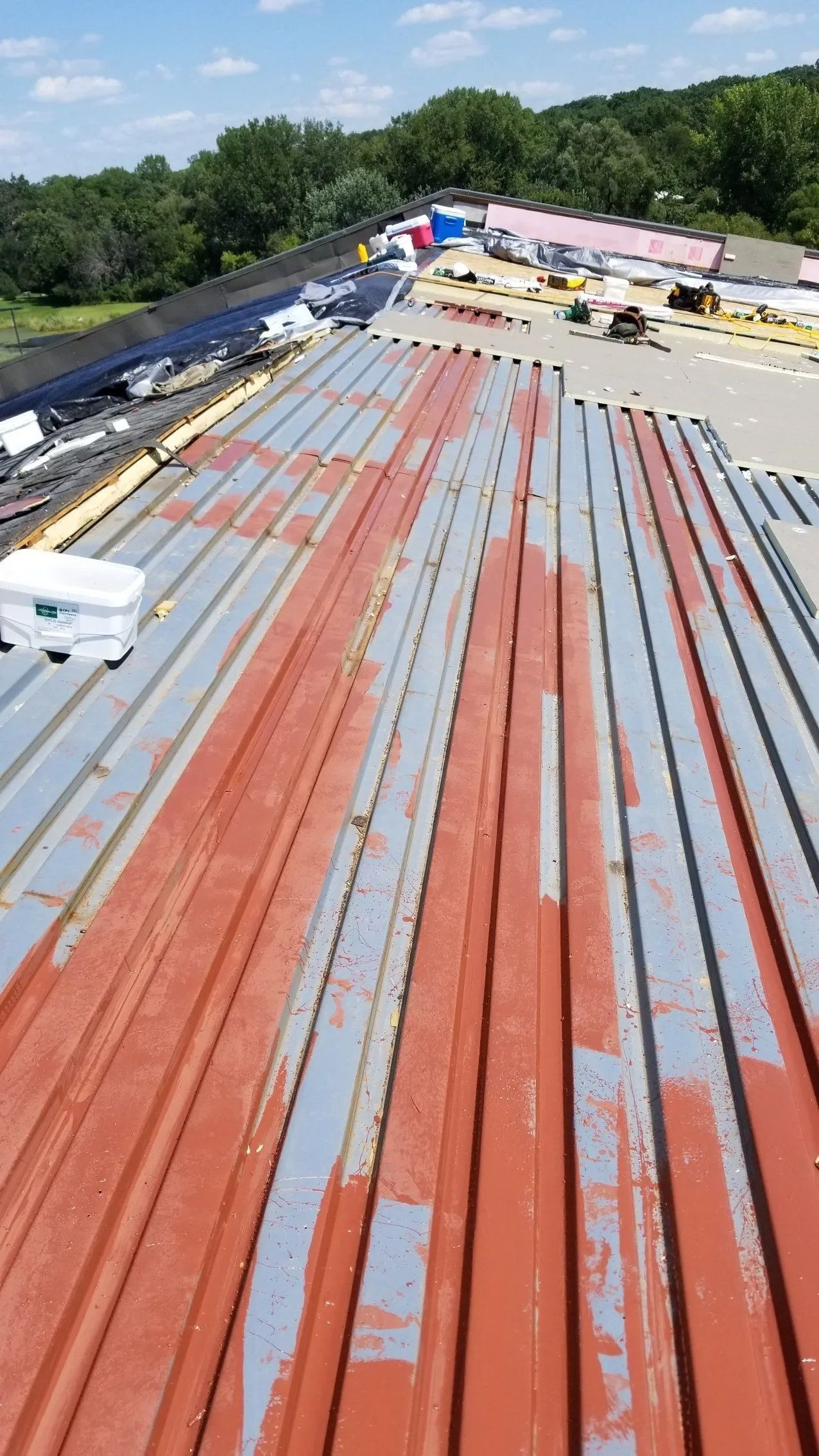Rusted metal roof panels on a building under construction, viewed from above with trees in the background