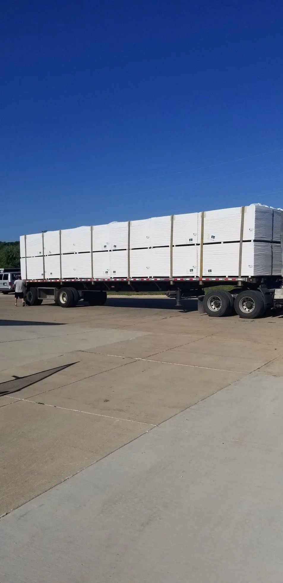 White flatbed truck carrying large white crates parked on a concrete lot under a clear blue sky