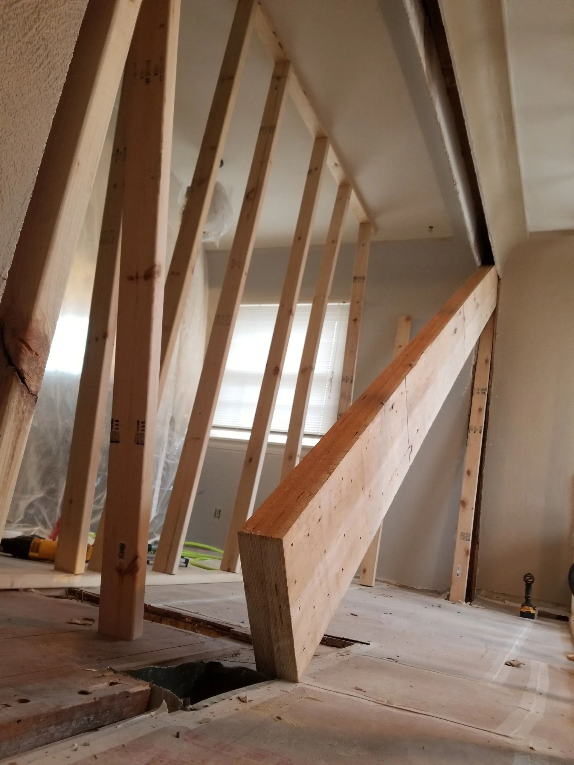 Broken wooden railing on an unfinished attic floor with exposed studs and daylight in the background