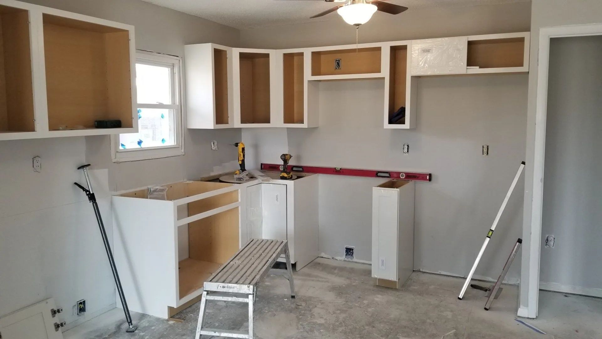 Renovated kitchen under construction with unfinished white cabinets, countertop supports, and tools on the floor