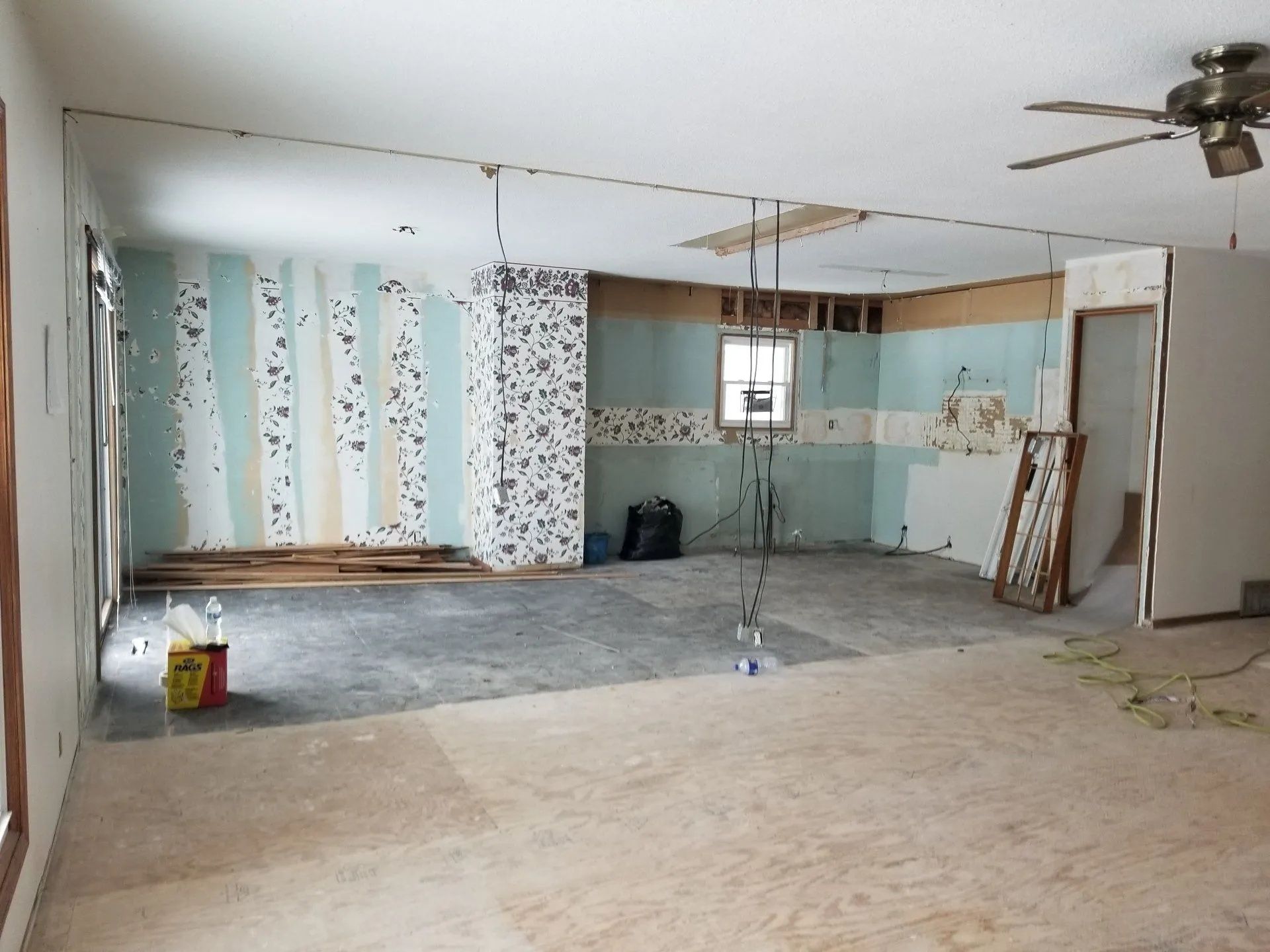 Partially gutted room with exposed walls, hanging ceiling wires, and construction materials on the floor