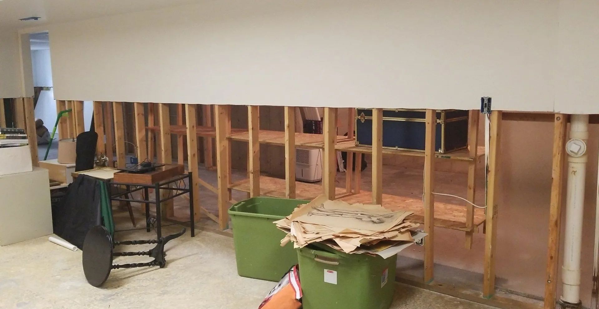 Partially demolished room with exposed wall studs, debris, and green bins on a tiled floor