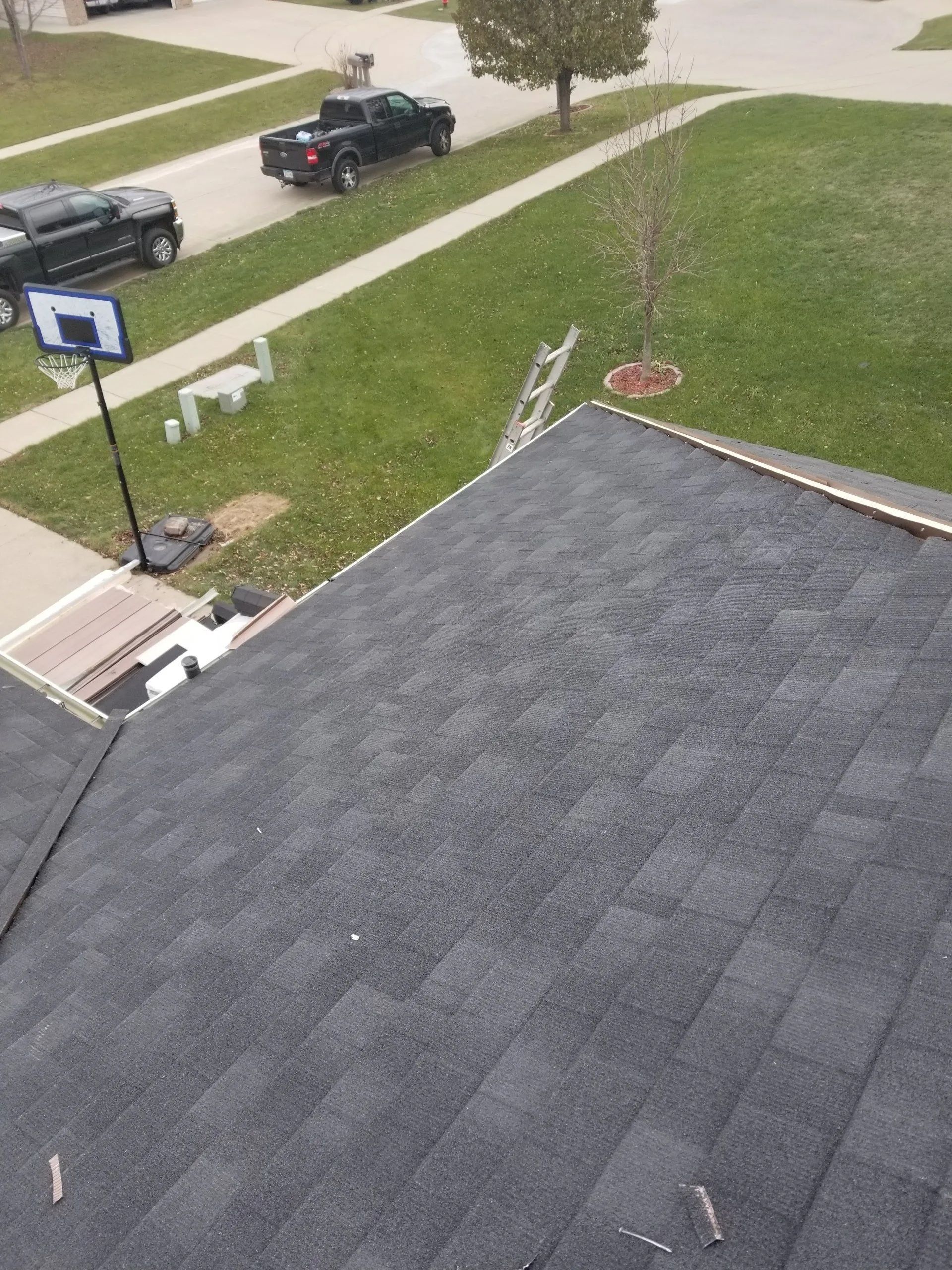 View from a rooftop over a suburban street, lawn, parked trucks, and a basketball hoop.