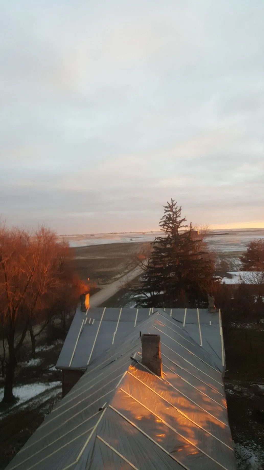 Sunset light on a rooftop with a chimney, overlooking trees and a distant river or bay
