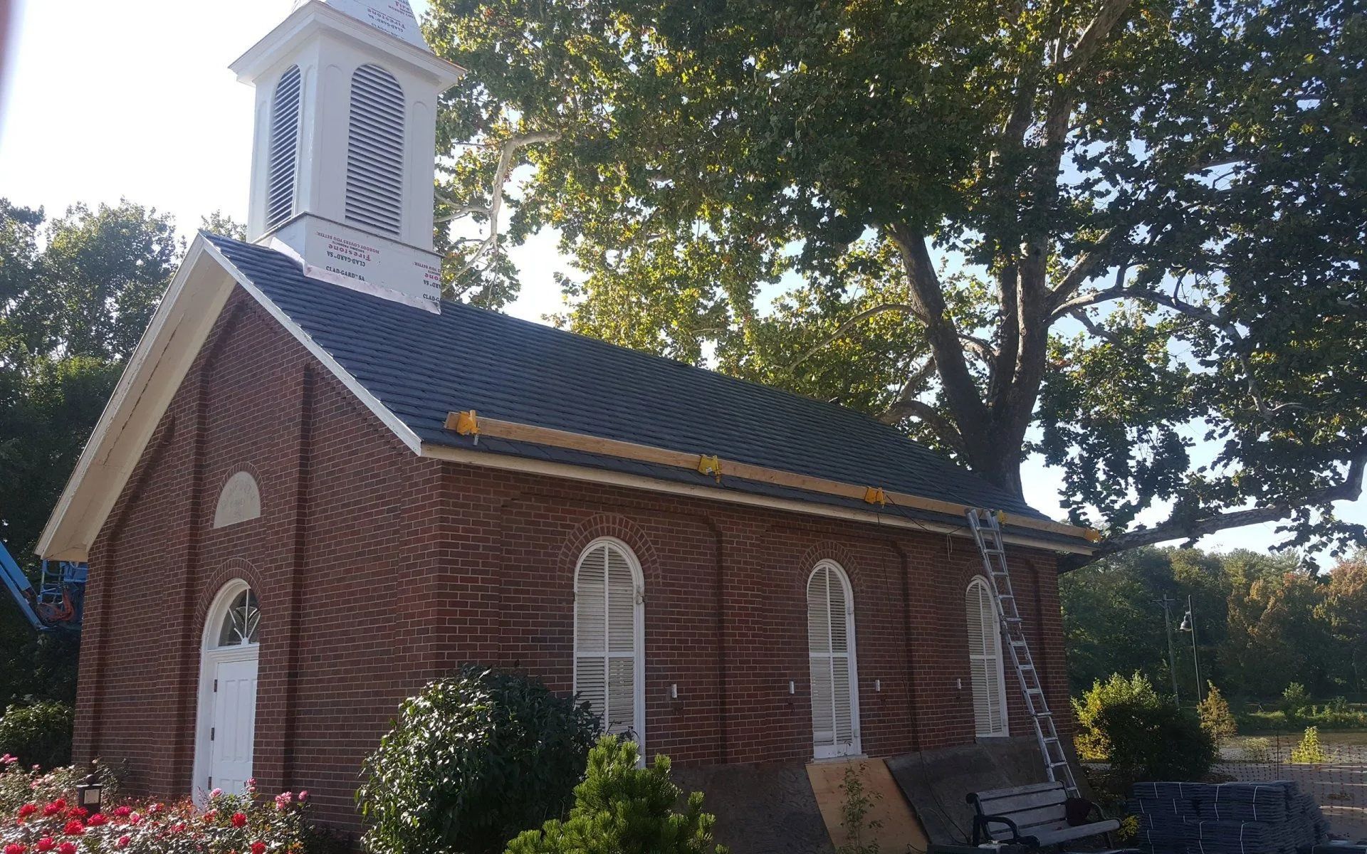 Small red-brick church with white trim and steeple, surrounded by trees in a sunny garden.