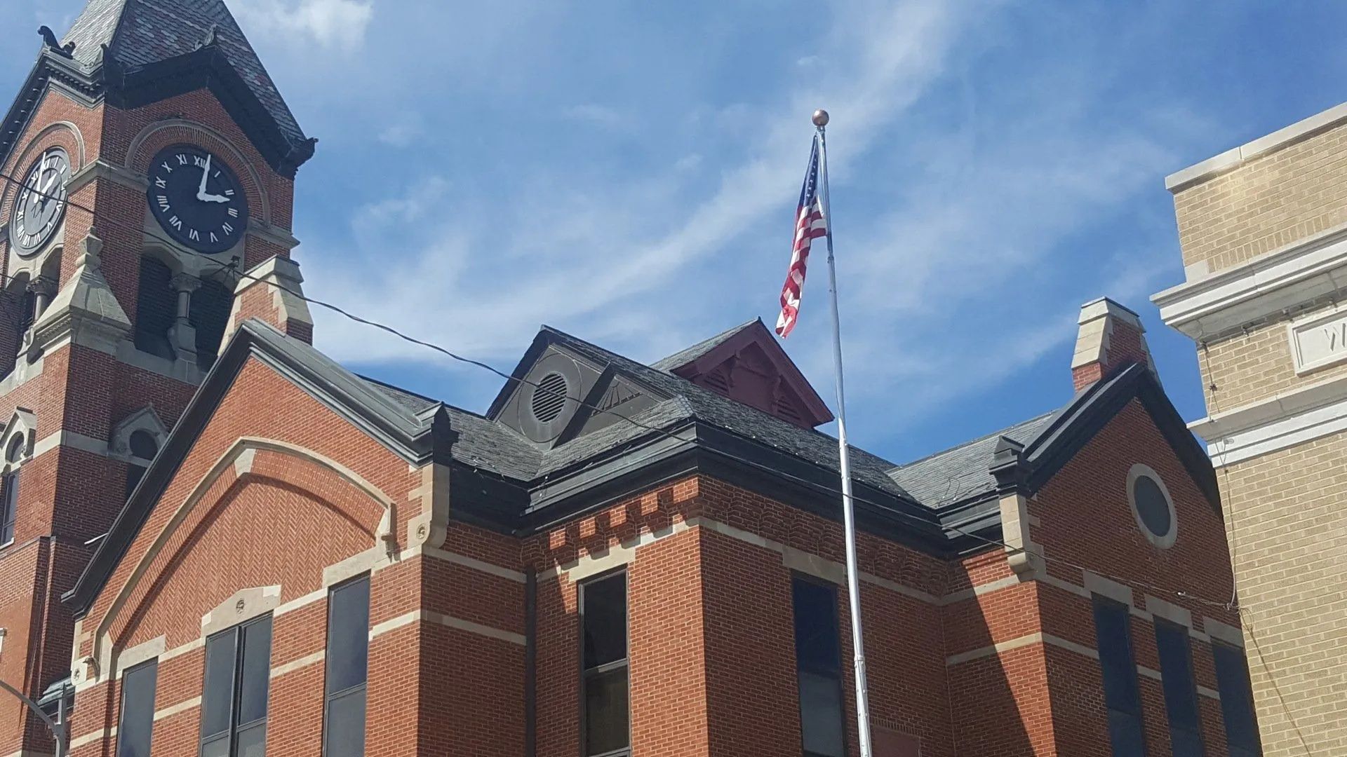 Brick civic building with a clock tower and American flag against a blue sky