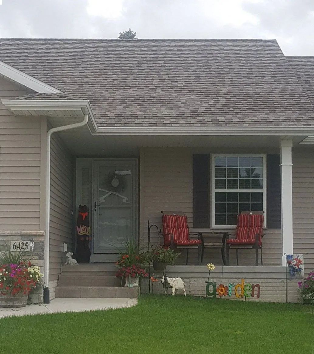 Front porch of a beige house with two red chairs, flower pots, and a green lawn