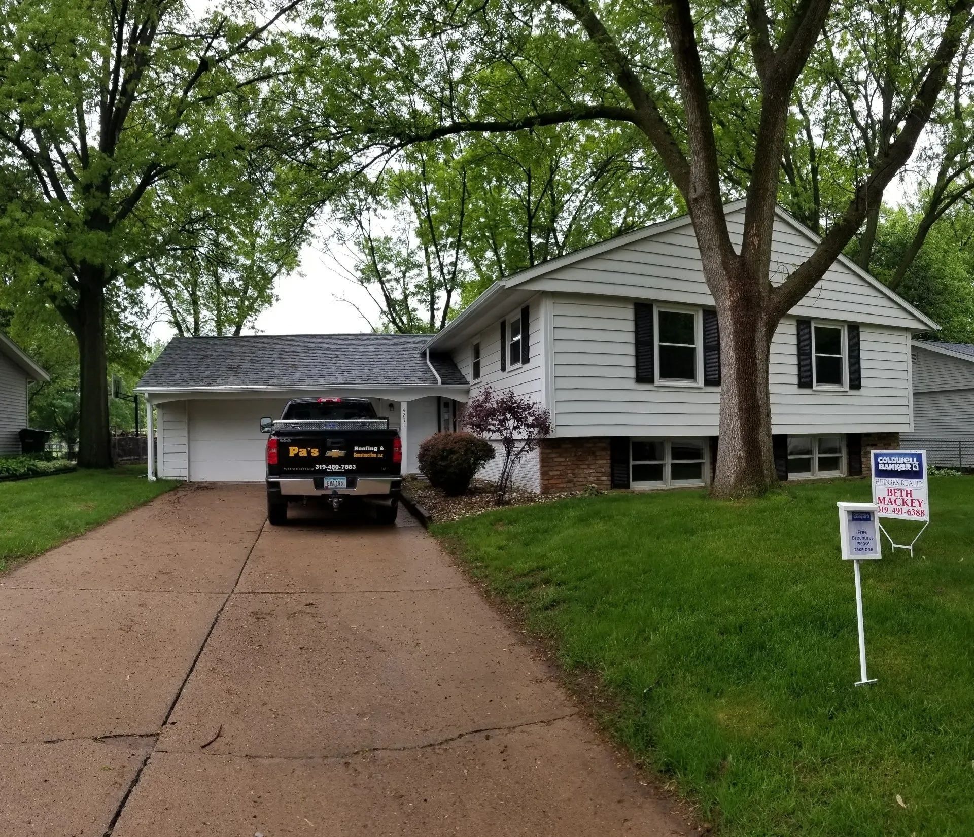 Suburban house with a black pickup in the driveway and a real estate sign on the lawn