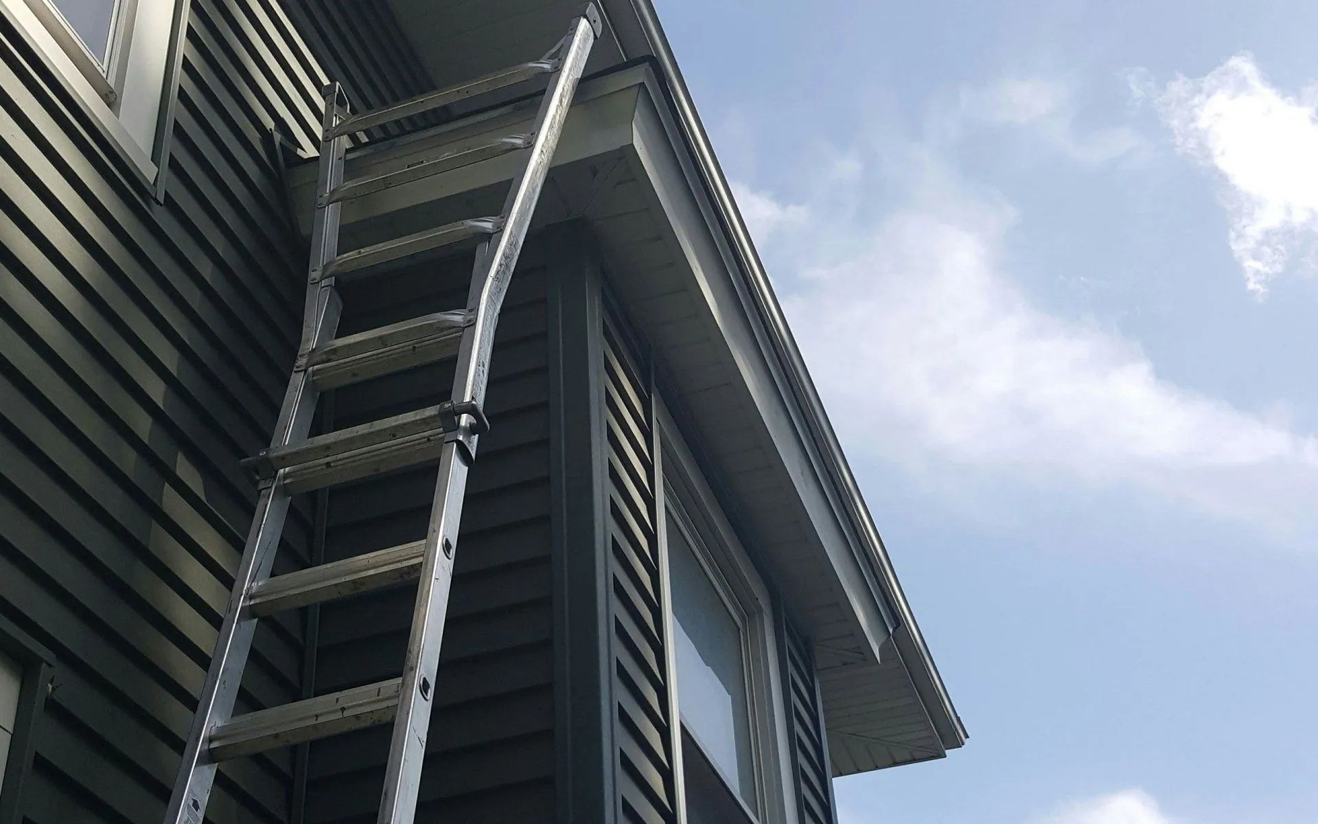 Low-angle view of a modern building corner with metal siding, windows, and overhanging roof against a blue sky
