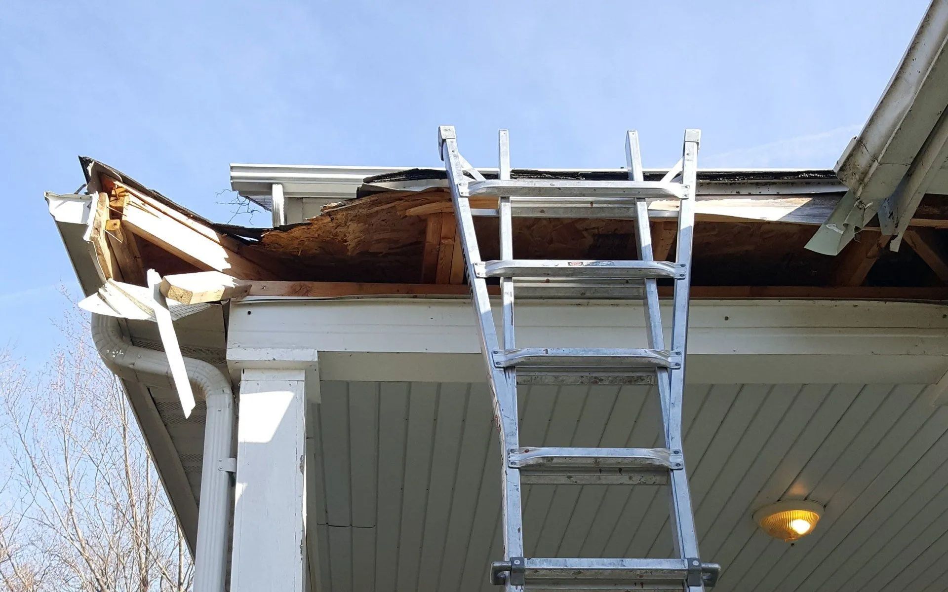 Ladder leaning against a house roof with damaged shingles and exposed underlayment