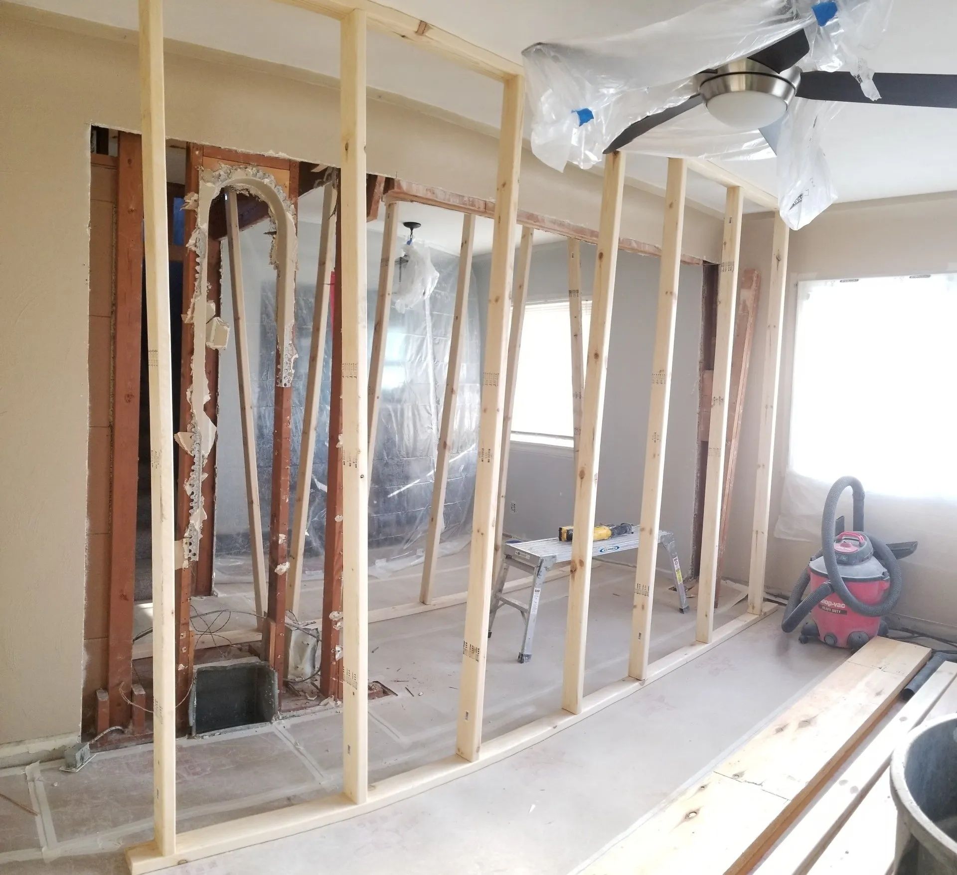 Partially framed interior wall under construction with exposed studs, plastic sheeting, and tools on the floor