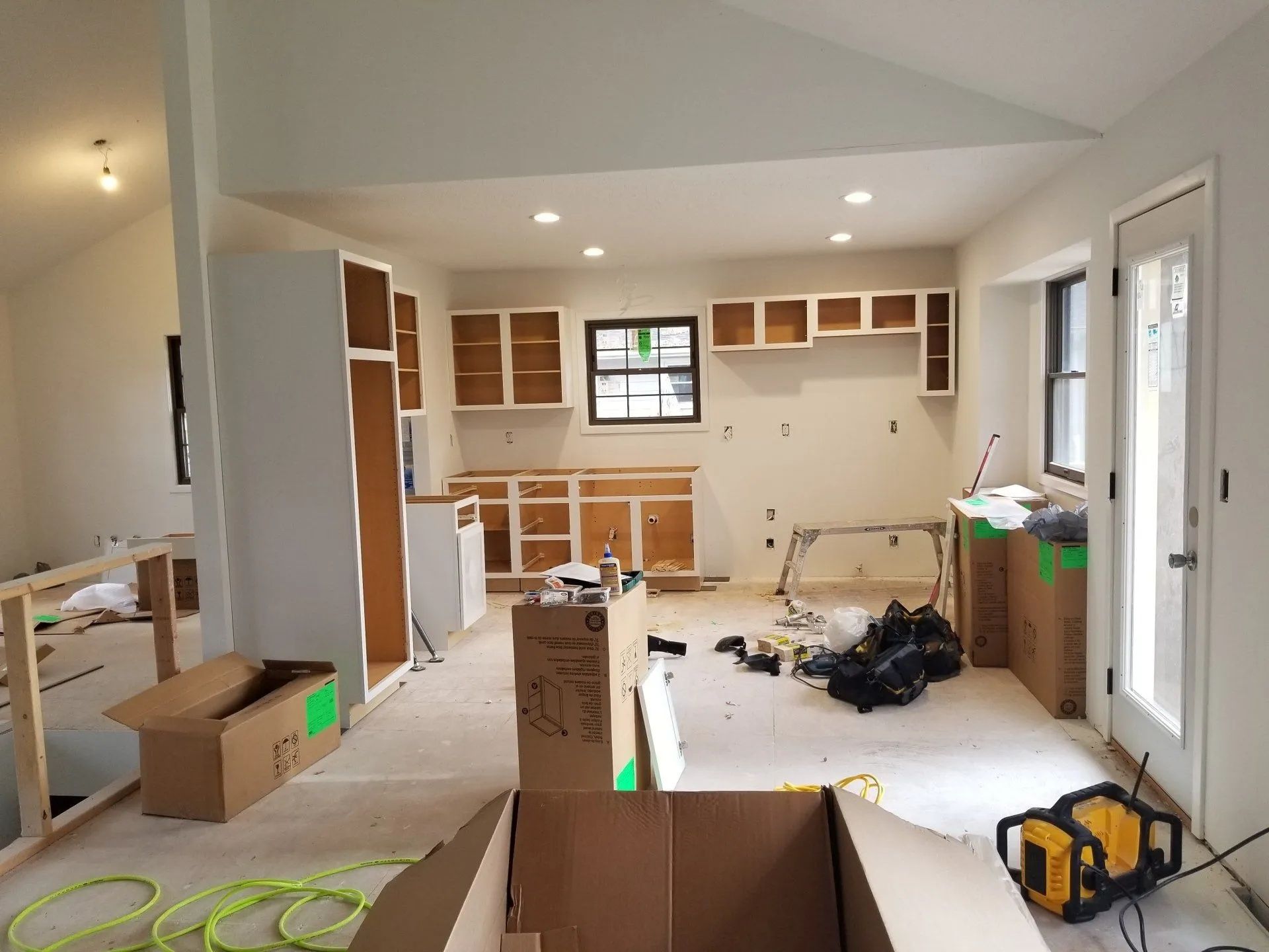 Renovated kitchen with unfinished cabinets, cardboard boxes, and construction tools on the floor