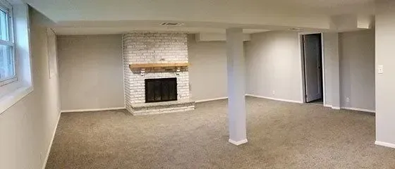 Empty carpeted living room with a white brick fireplace, support column, and large windows