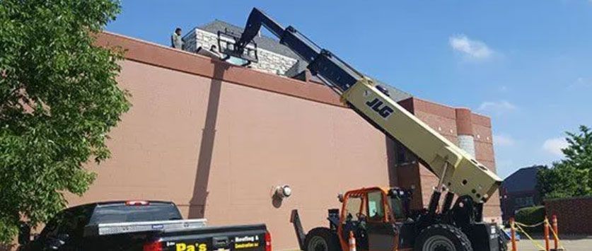 Yellow crane lifting materials over a building with workers below on a sunny day