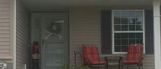 Front porch with a gray door, window, and two red chairs on a house exterior.