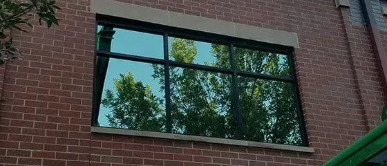 Brick building with a dark-framed window reflecting trees and blue sky