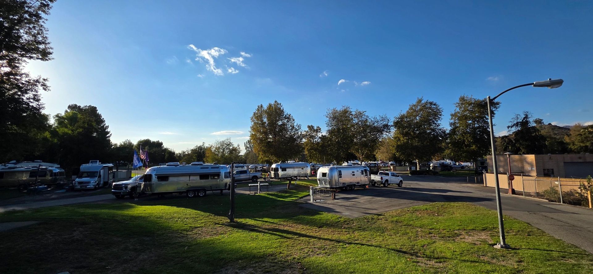 Campground with RVs parked on grass under a clear blue sky. Trees surround the area.
