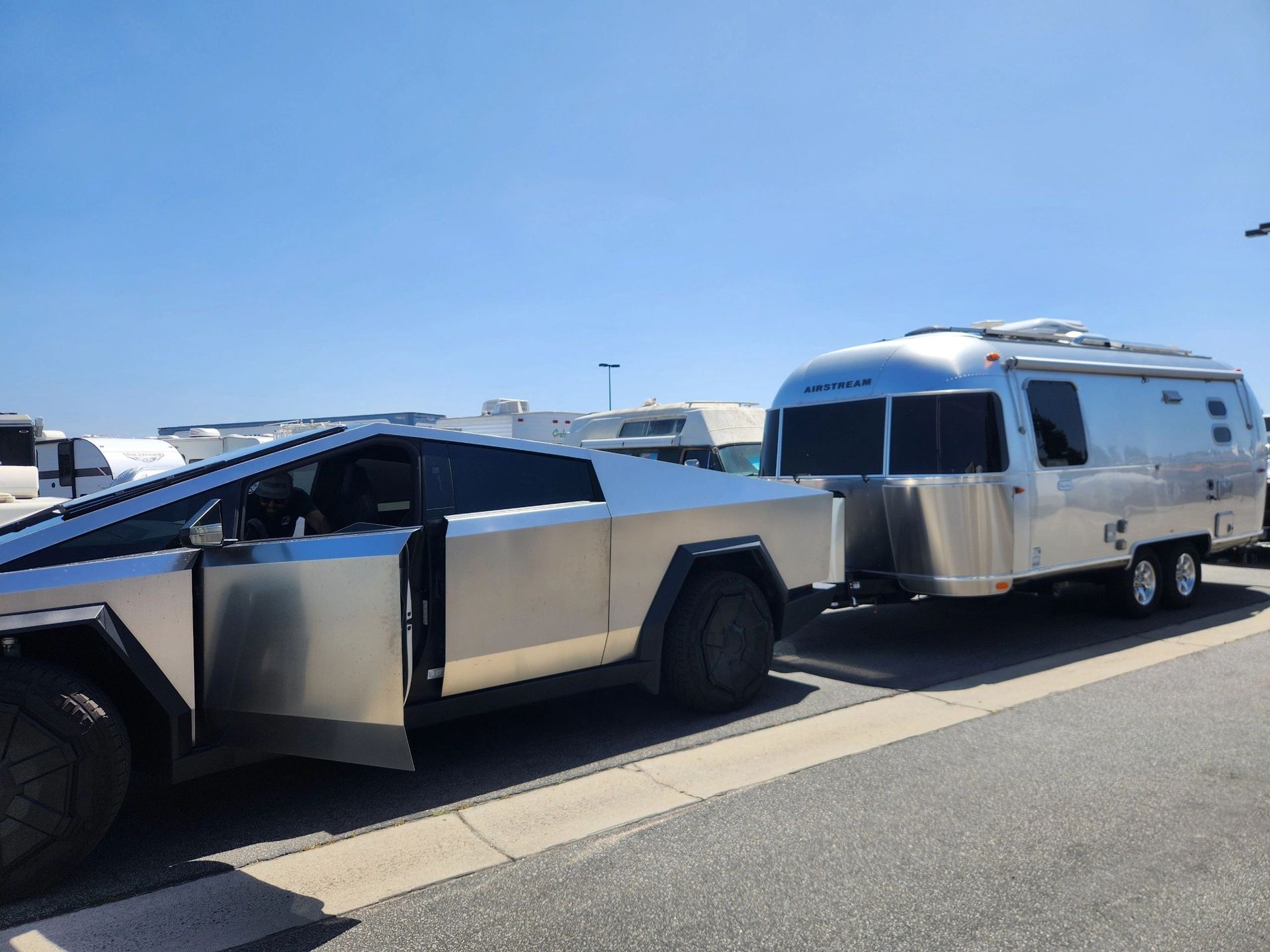 Tesla Cybertruck towing a silver Airstream trailer on a sunny day.
