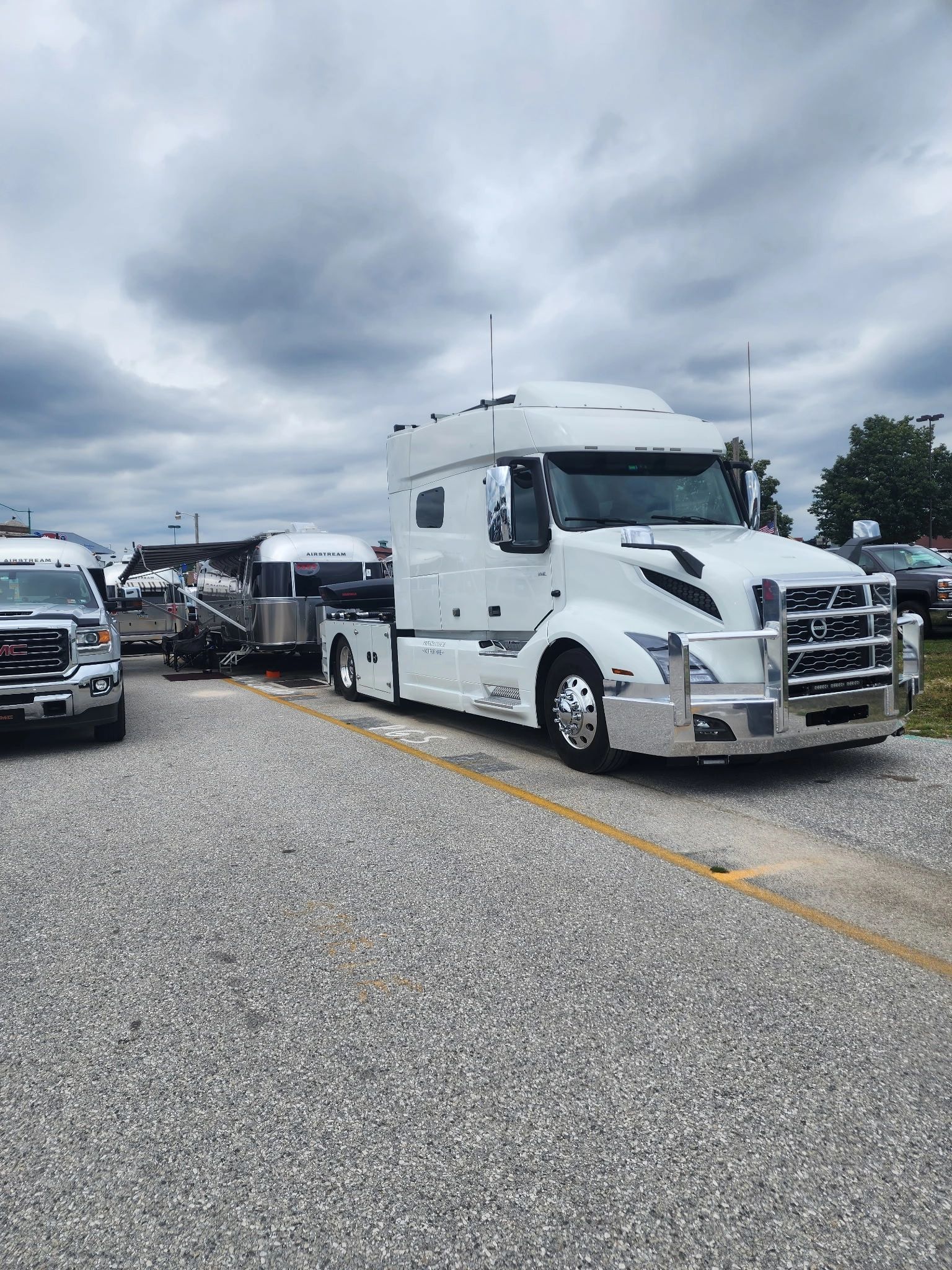 White semi-truck with chrome grill parked on gravel, pulling a trailer on a cloudy day.