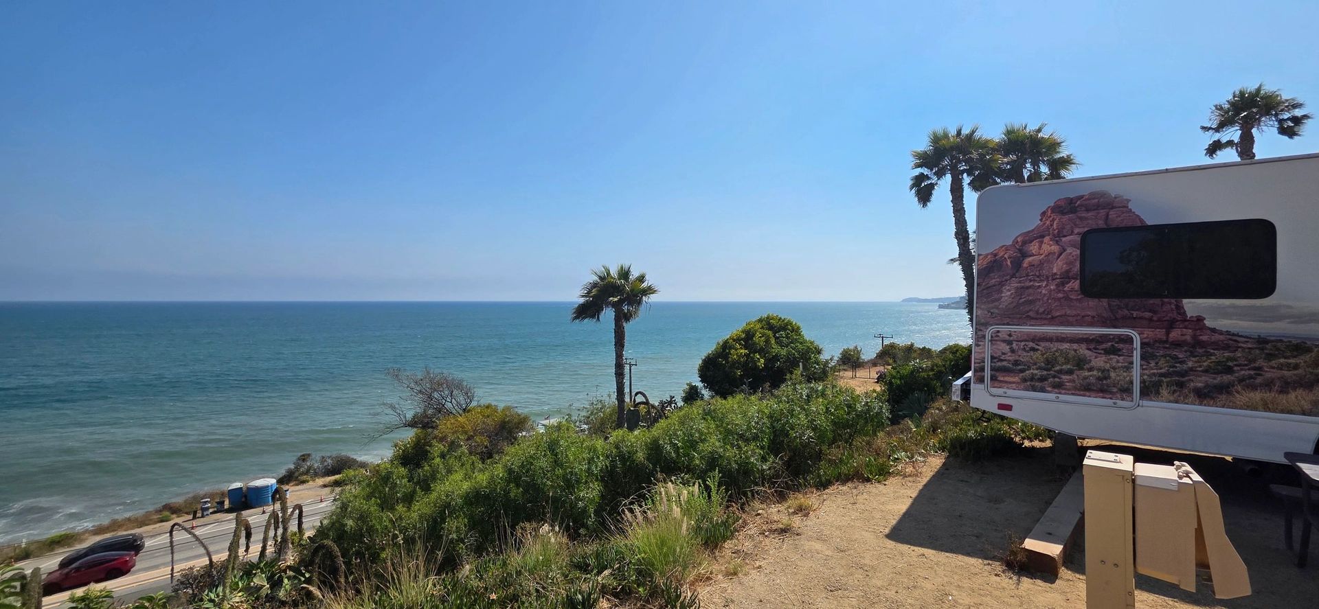 RV parked overlooking the ocean, with trees and a clear blue sky.