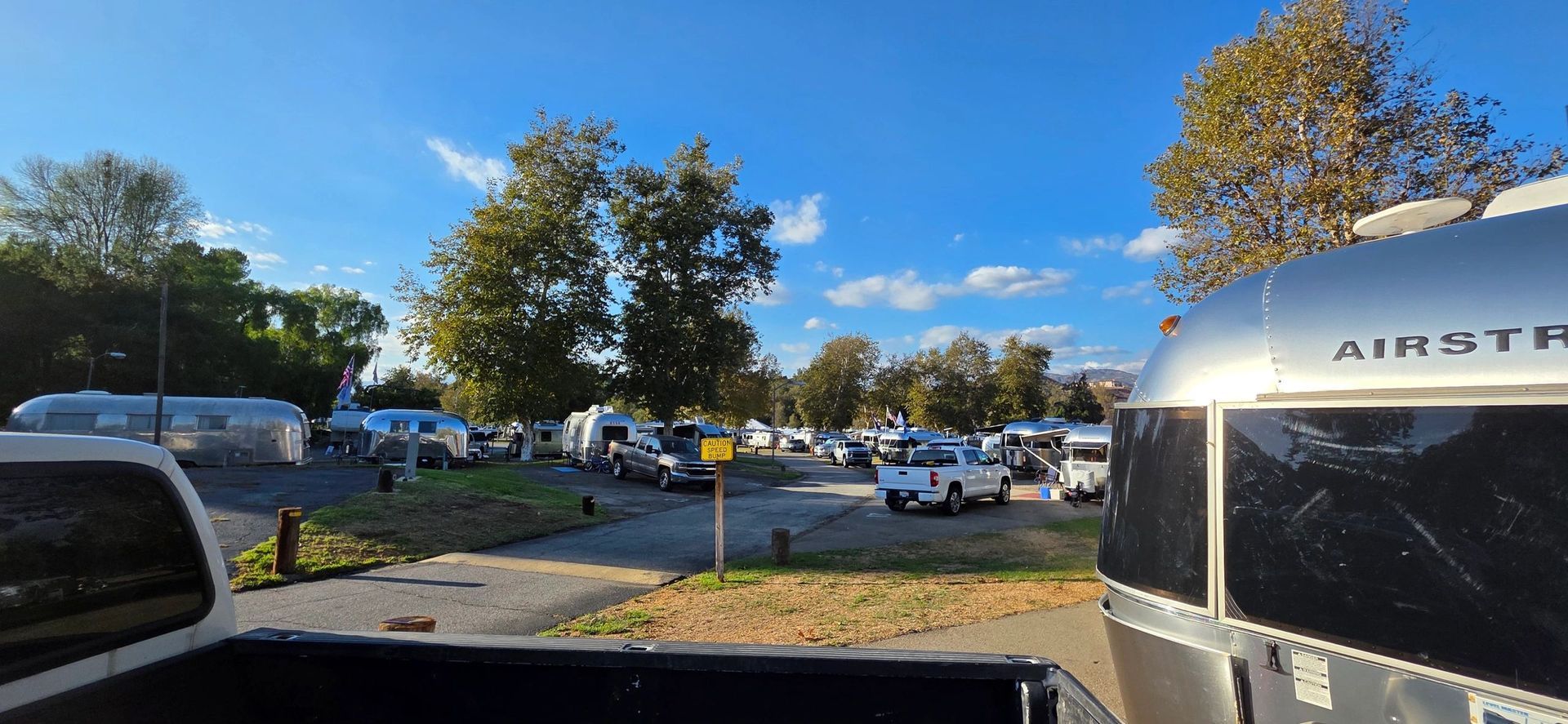 An RV park with trailers and trucks under a blue sky. Airstream trailer in foreground.