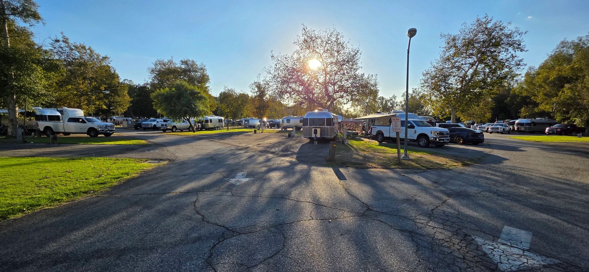 Campground scene with parked vehicles and trees under a sunny sky.