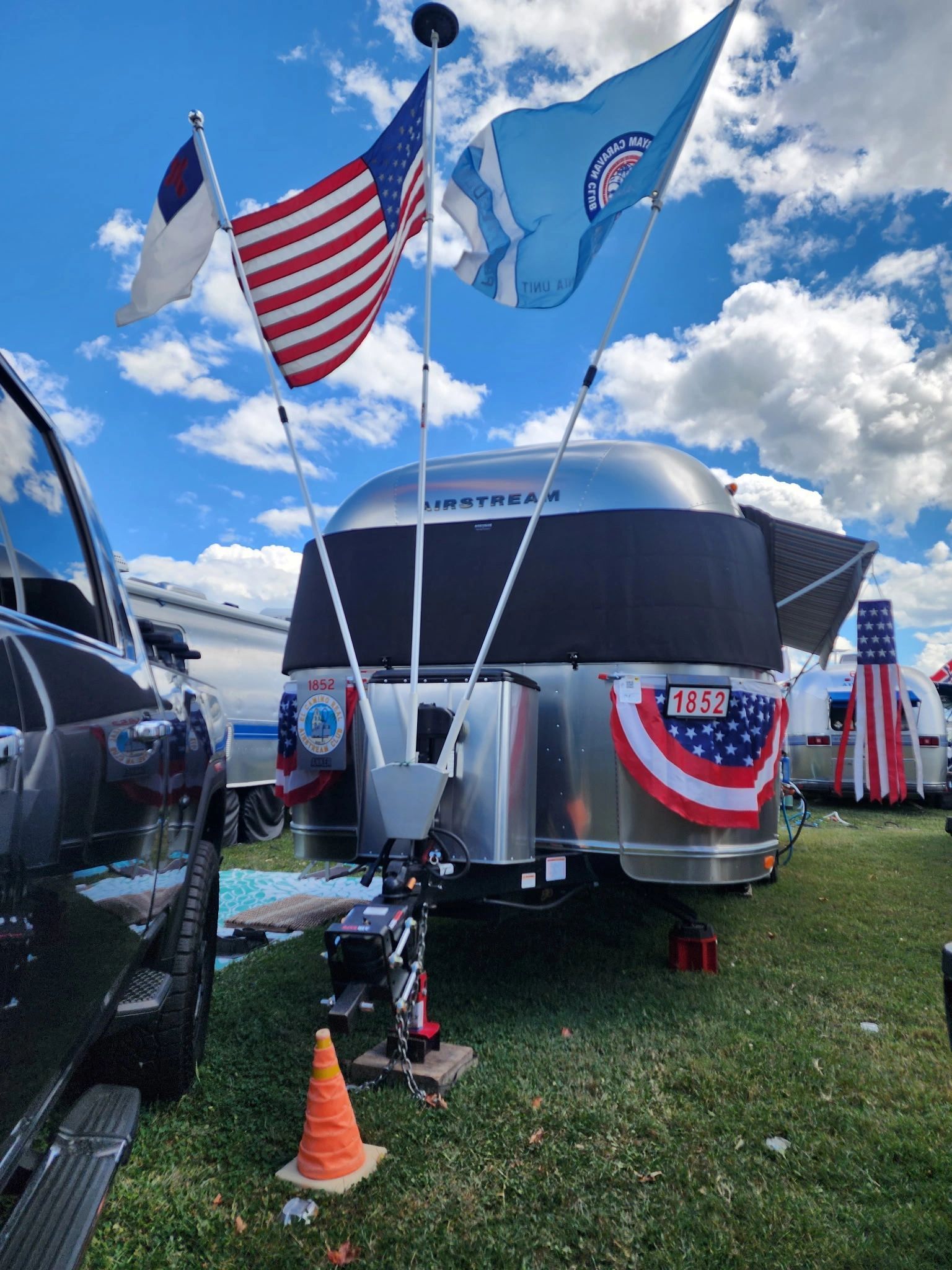 An Airstream trailer with American, Christian, and blue flags. It's on a grassy field on a sunny day.