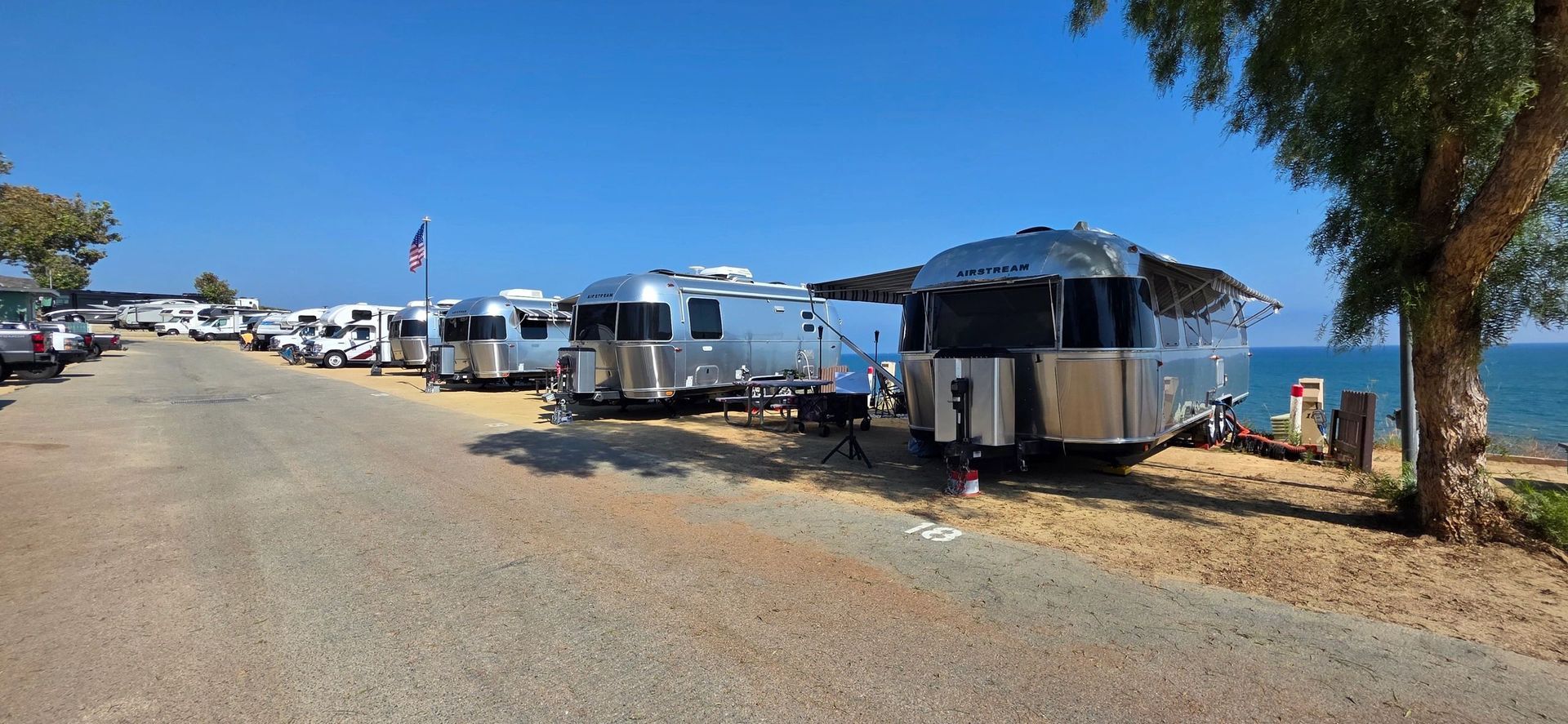 A line of silver RVs parked along a beach road under a clear blue sky.