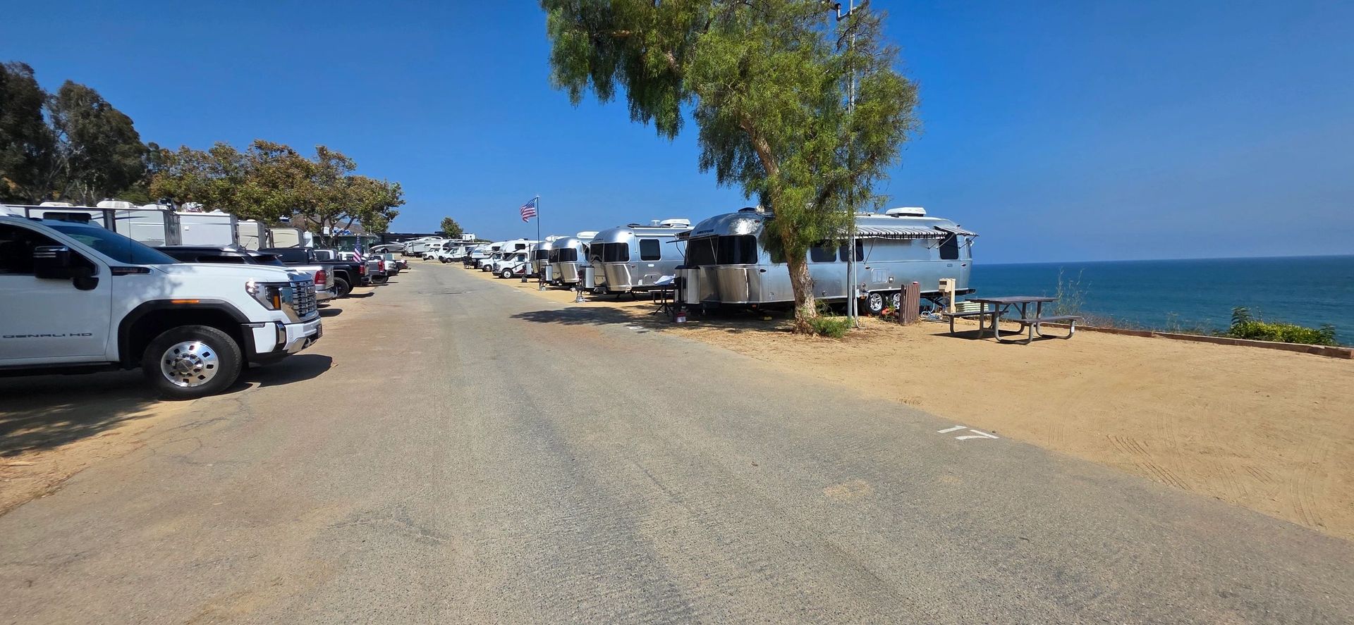 Campground with Airstream trailers and trucks along a gravel road near the ocean on a sunny day.