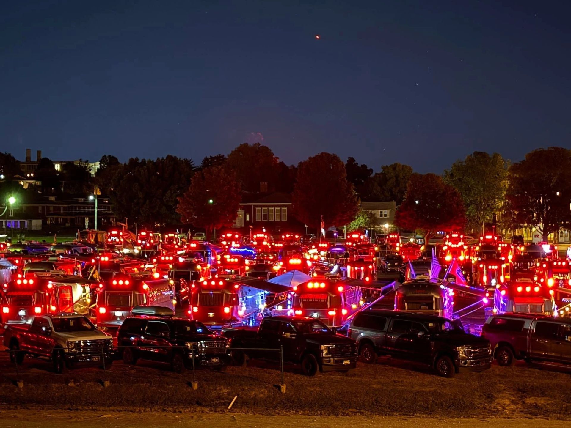 Night shot of numerous red trucks lit up, parked in a lot, possibly for a parade or display.