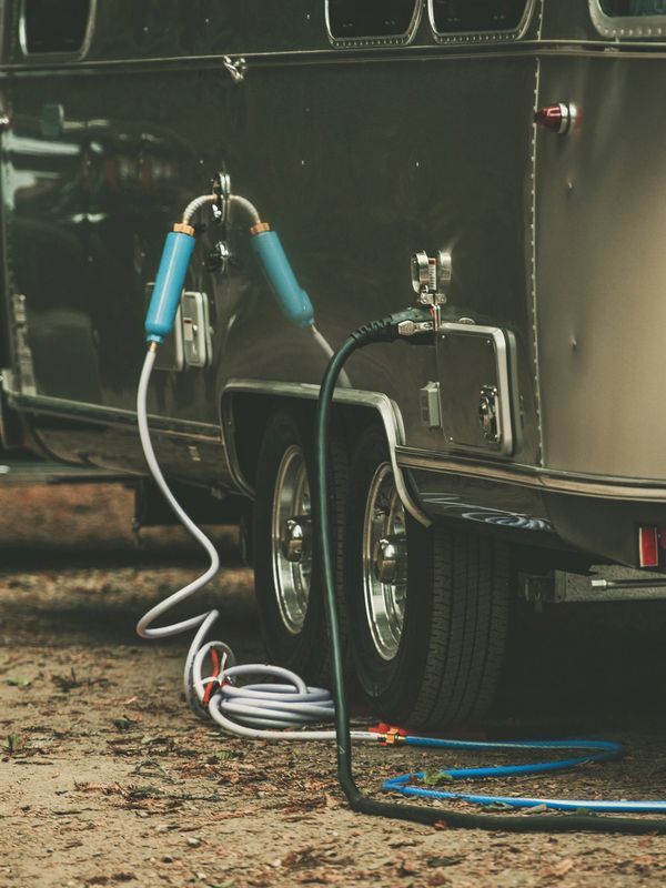 Airstream trailer with water hose and blue water filter attached near the tires.