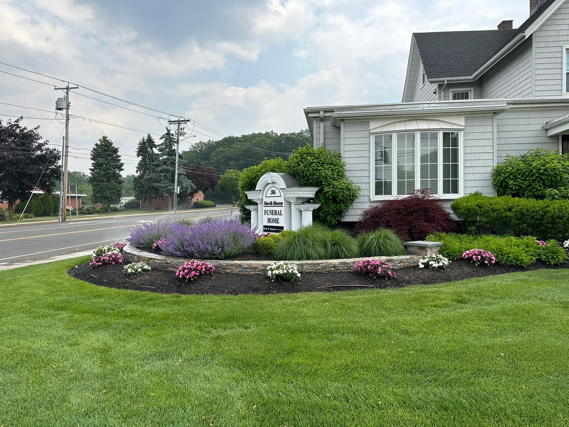A white house with a lush green lawn and flowers in front of it.