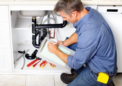 Plumber fixing under-sink pipes with tools in a kitchen cabinet