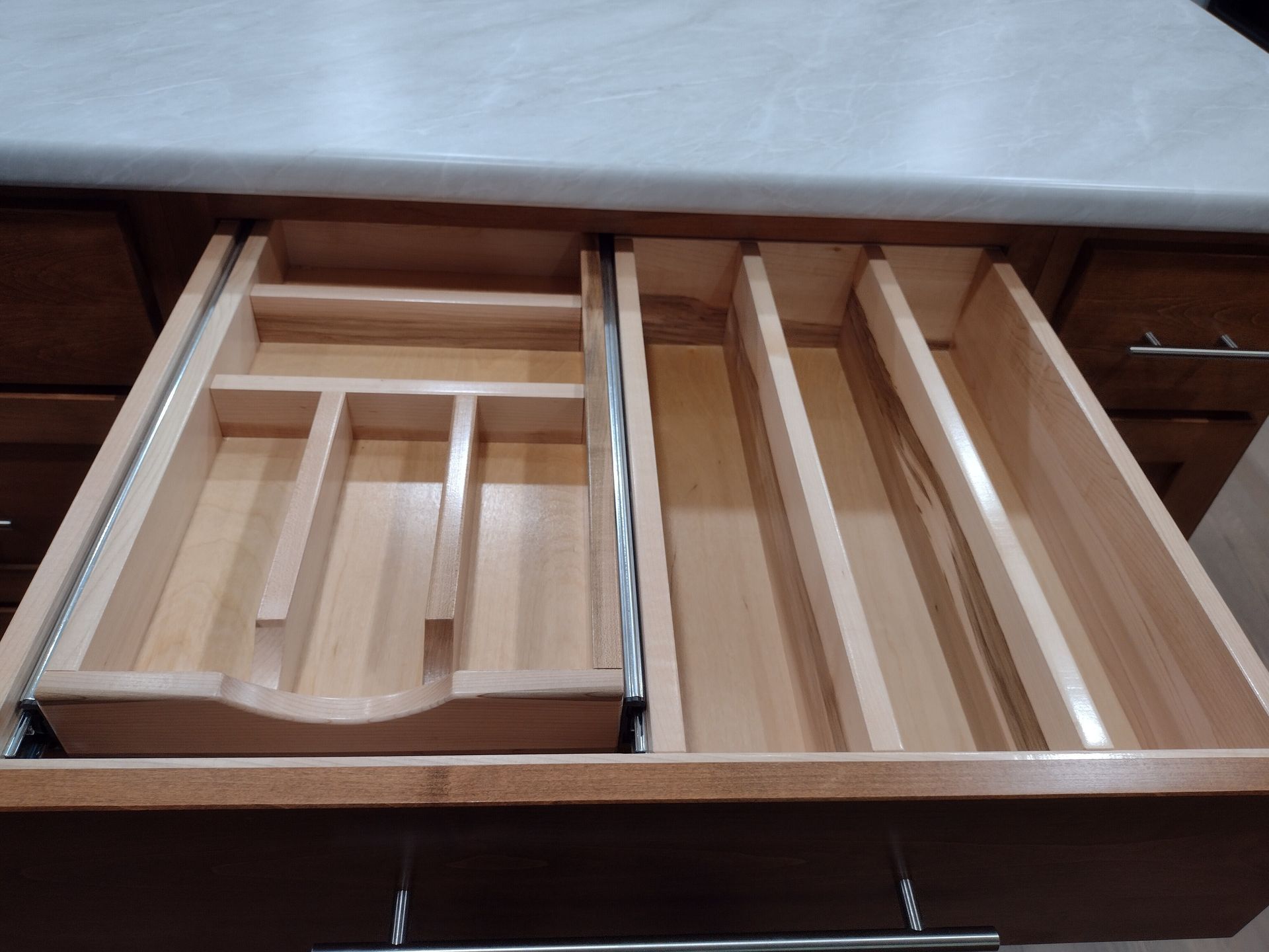 Wooden kitchen drawer with cutlery dividers and long, narrow compartments, open and ready to be filled.