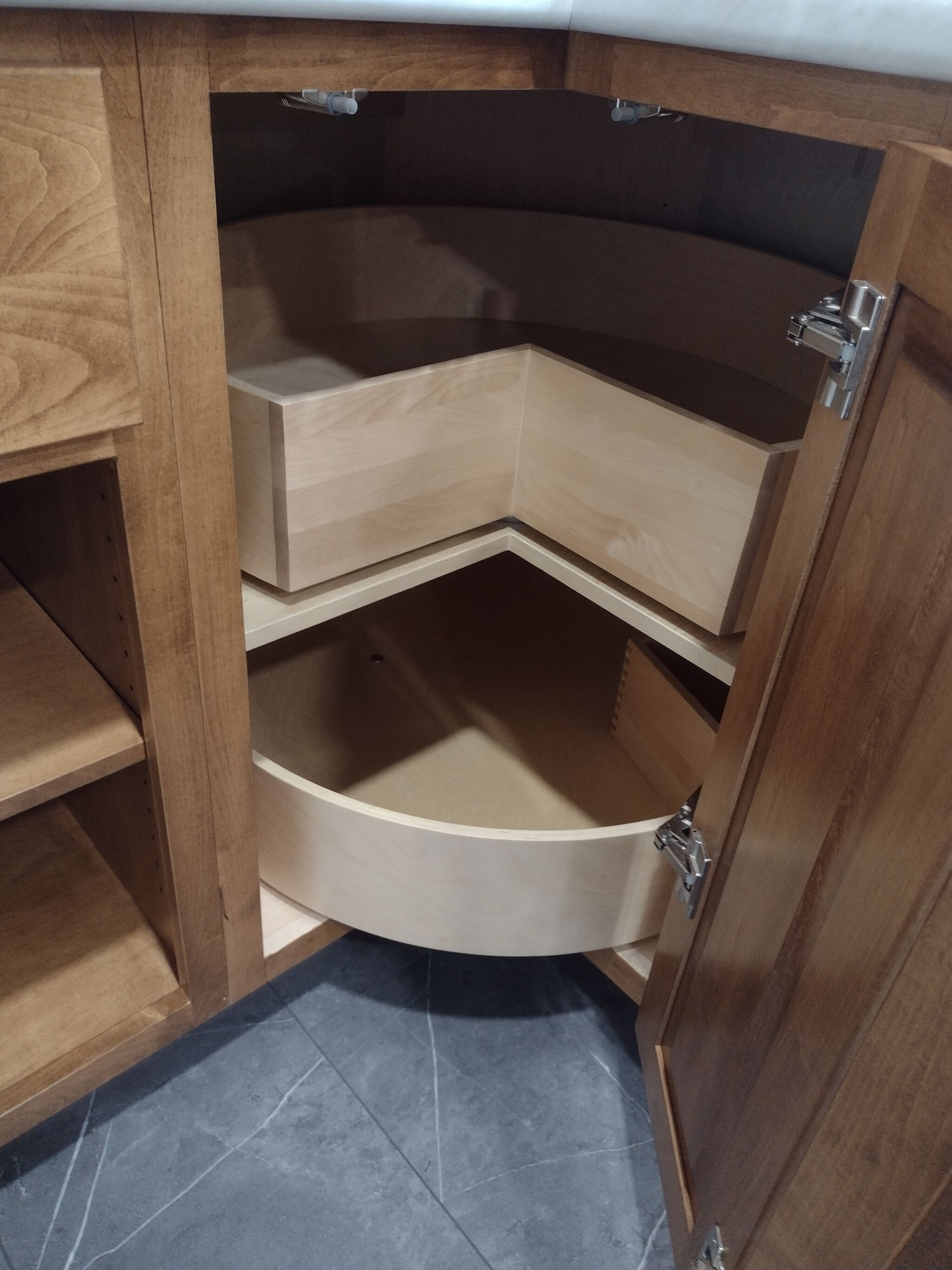 Wooden kitchen cabinet open to reveal two-tiered corner storage: a sliding, rectangular drawer above a rotating, semi-circular shelf.