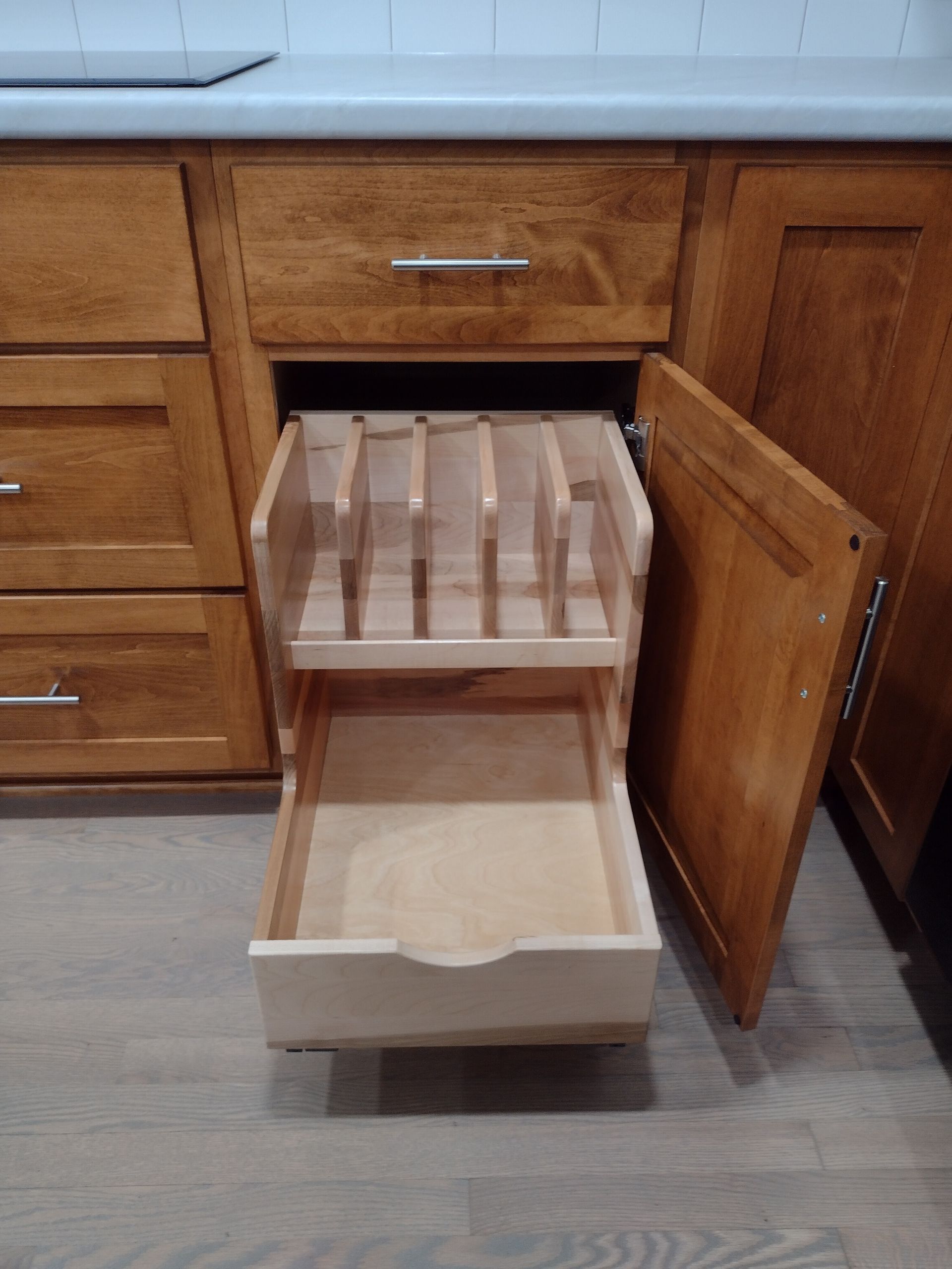 A pull-out kitchen cabinet with a wooden divider and drawer, displayed open. The wood is stained a warm brown color.