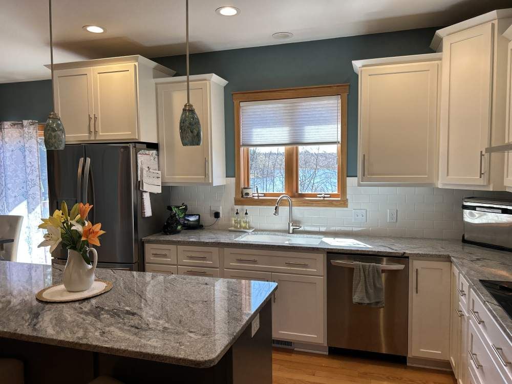 A kitchen with white cabinets, granite counter tops, stainless steel appliances and a large island.