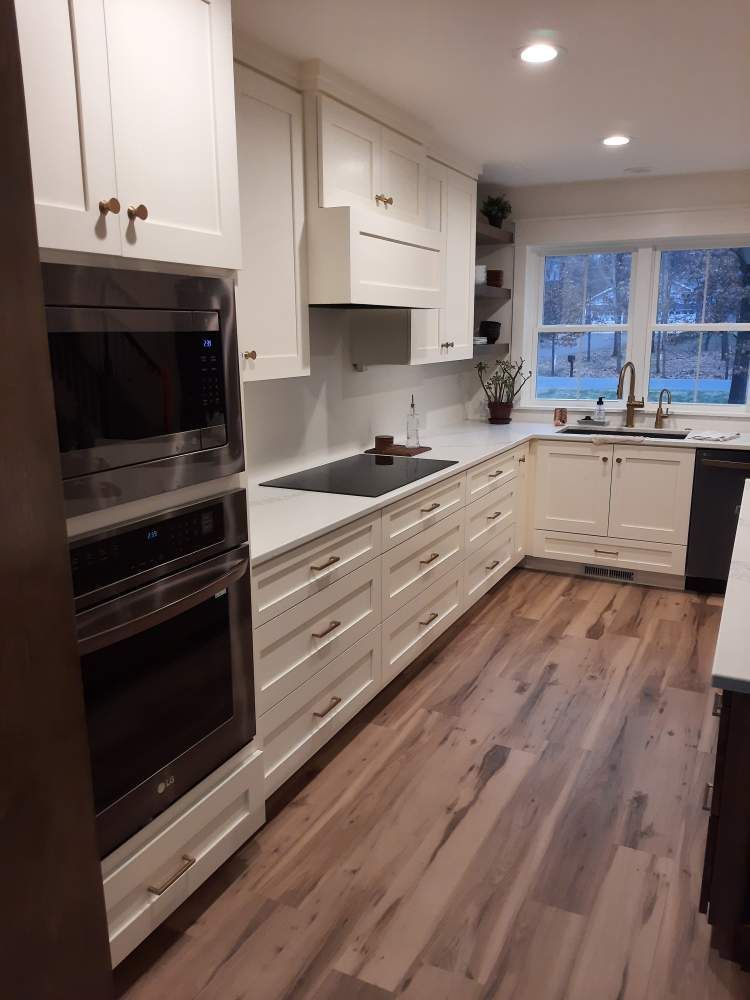 A kitchen with white cabinets, hardwood floors, stainless steel appliances and a window.