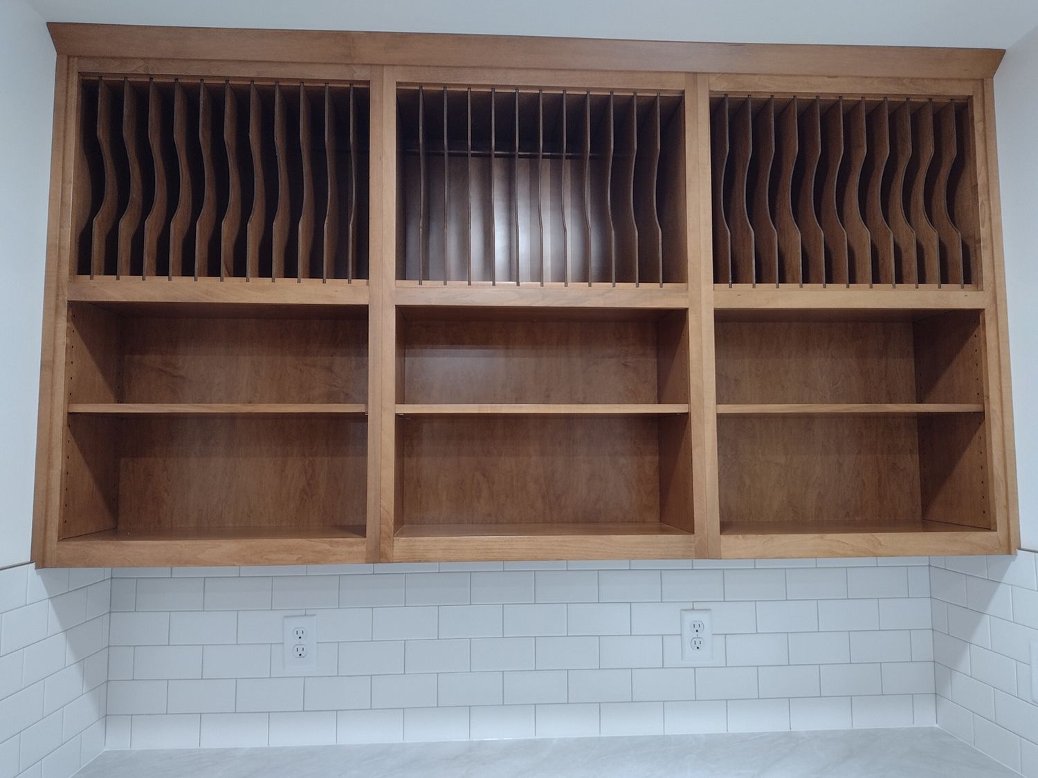 Wooden kitchen cabinet with plate racks above shelves, mounted above white tile backsplash.