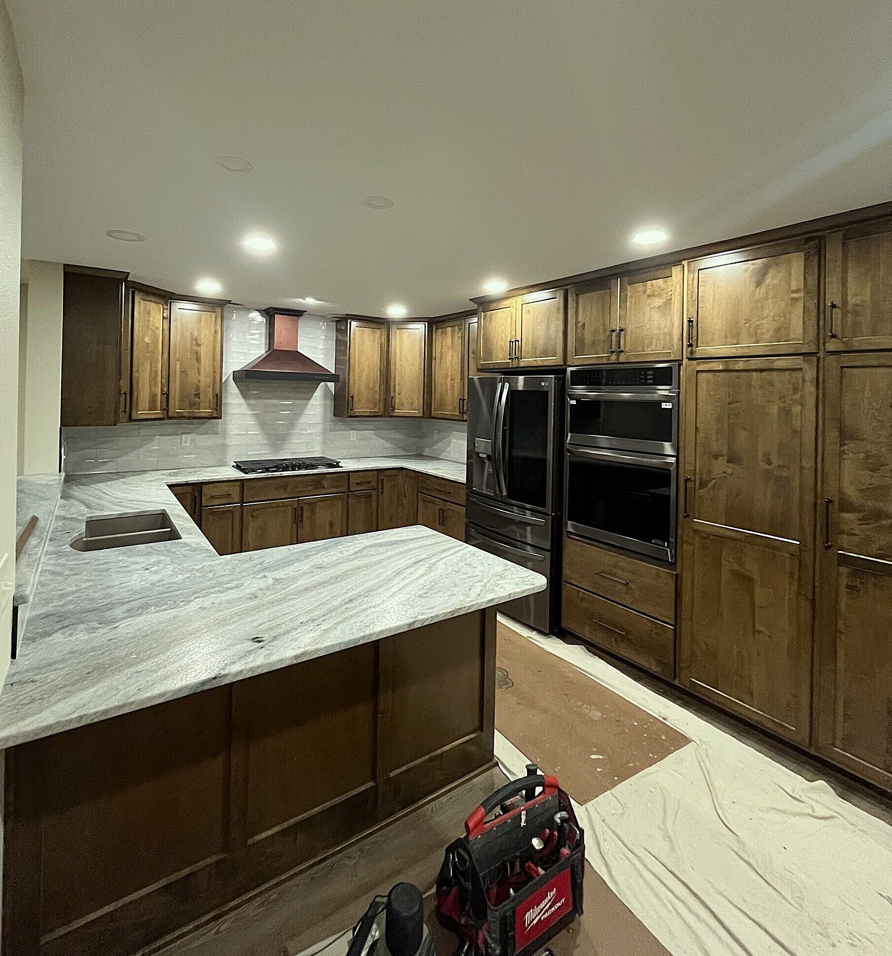 A newly renovated kitchen with wood cabinets, granite countertops, and stainless steel appliances. A toolbox sits on the floor.