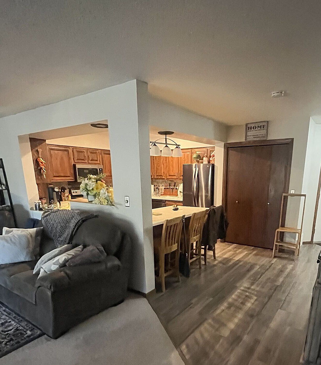 Open-concept living space with a kitchen partially visible. A gray couch sits near a half-wall. Wooden floors.